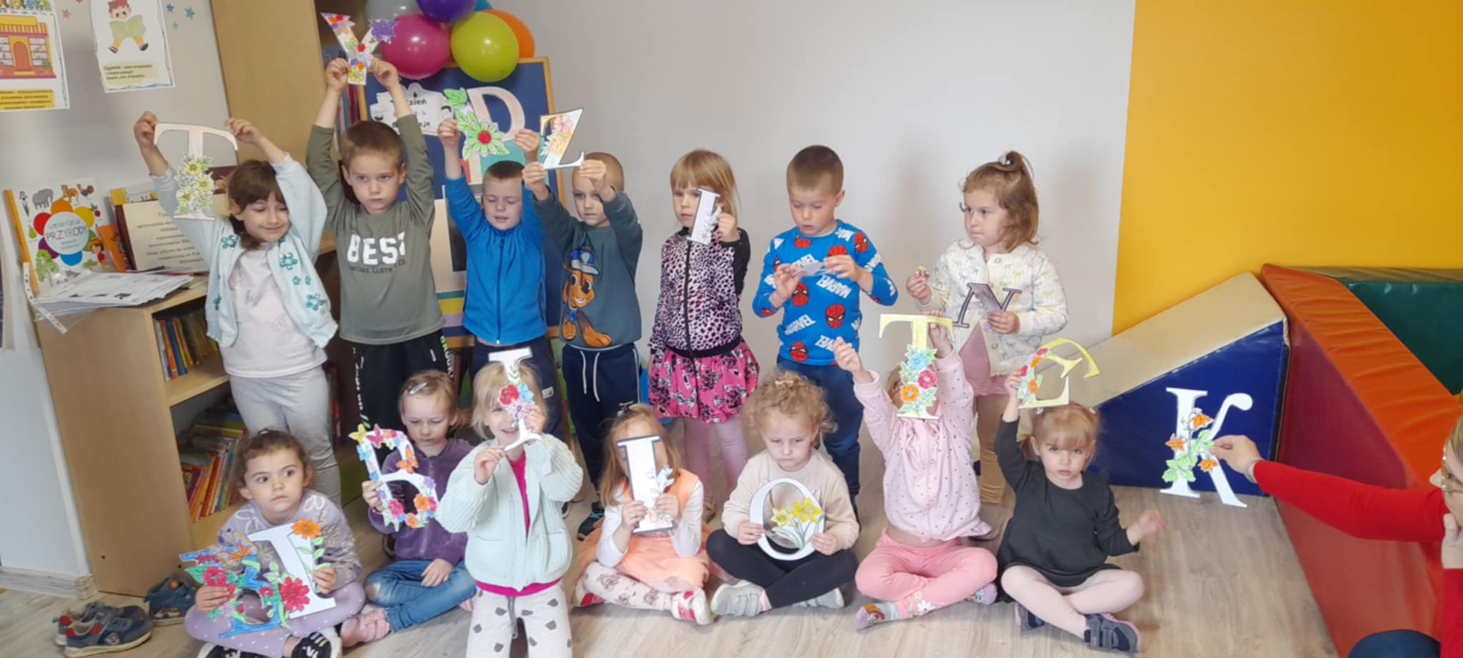 Na zdjęciu widoczna jest grupa dzieci trzymająca litery, które tworzą napis &quot;Tydzień  bibliotek&quot;.