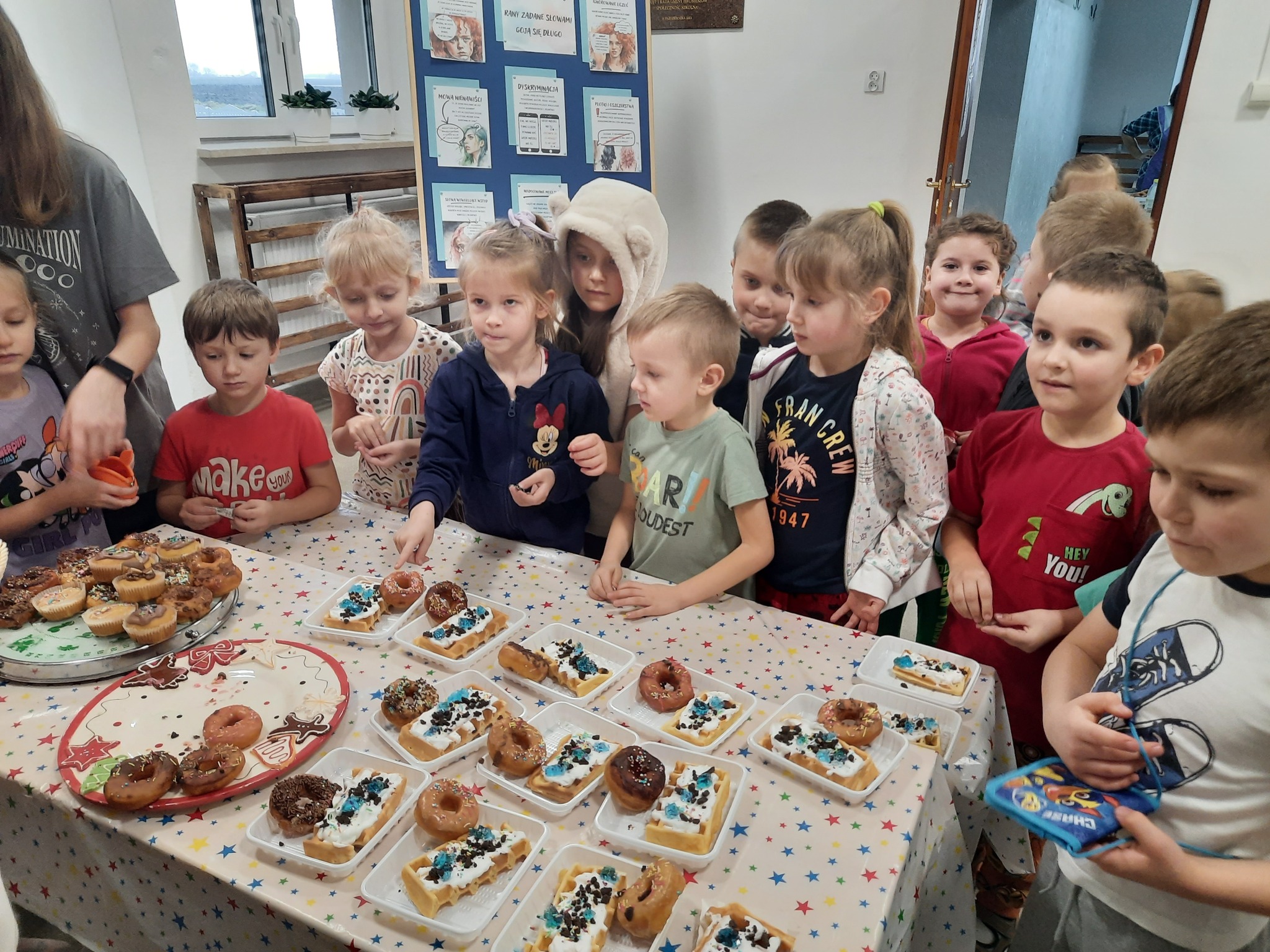 Dzieci ze starszej grupy przedszkolnej przy stole z goframi i pączkami