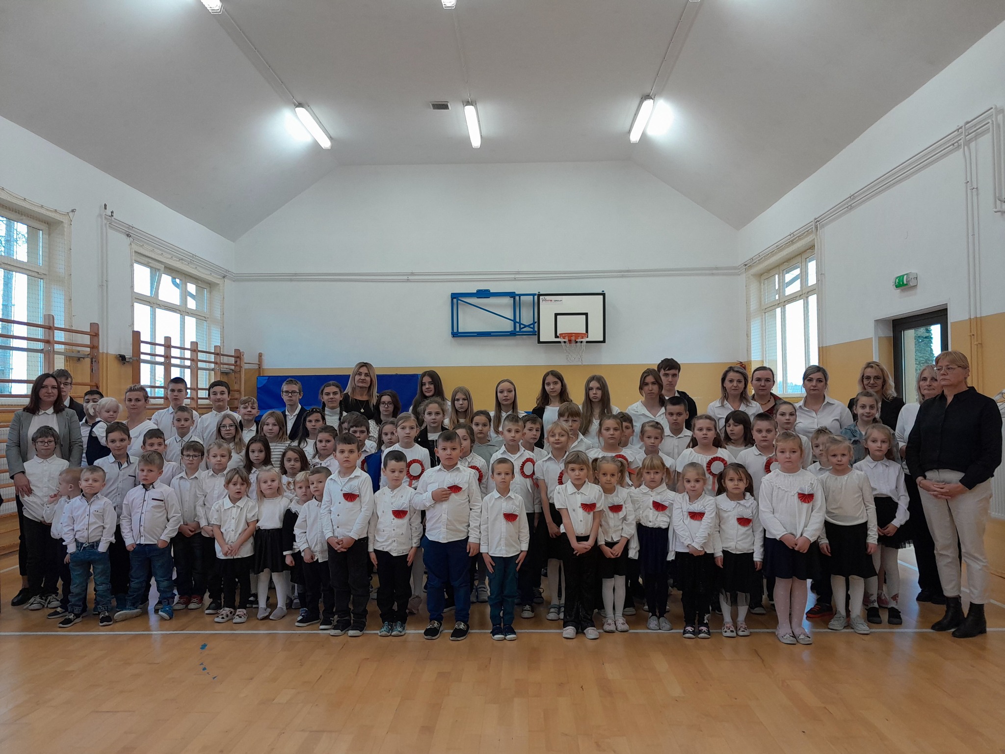 Uczniowie i nauczyciele w strojach galowych podczas śpiewania hymnu państwowego