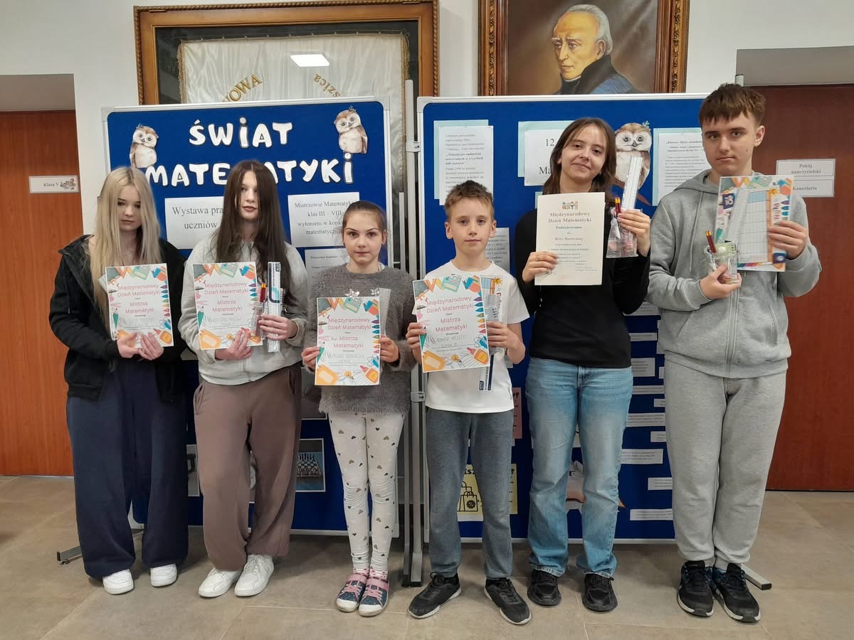Kilku uczniów z dyplomami i upominkami stoi na tle dekoracji dotyczącej Dnia Matematyki
