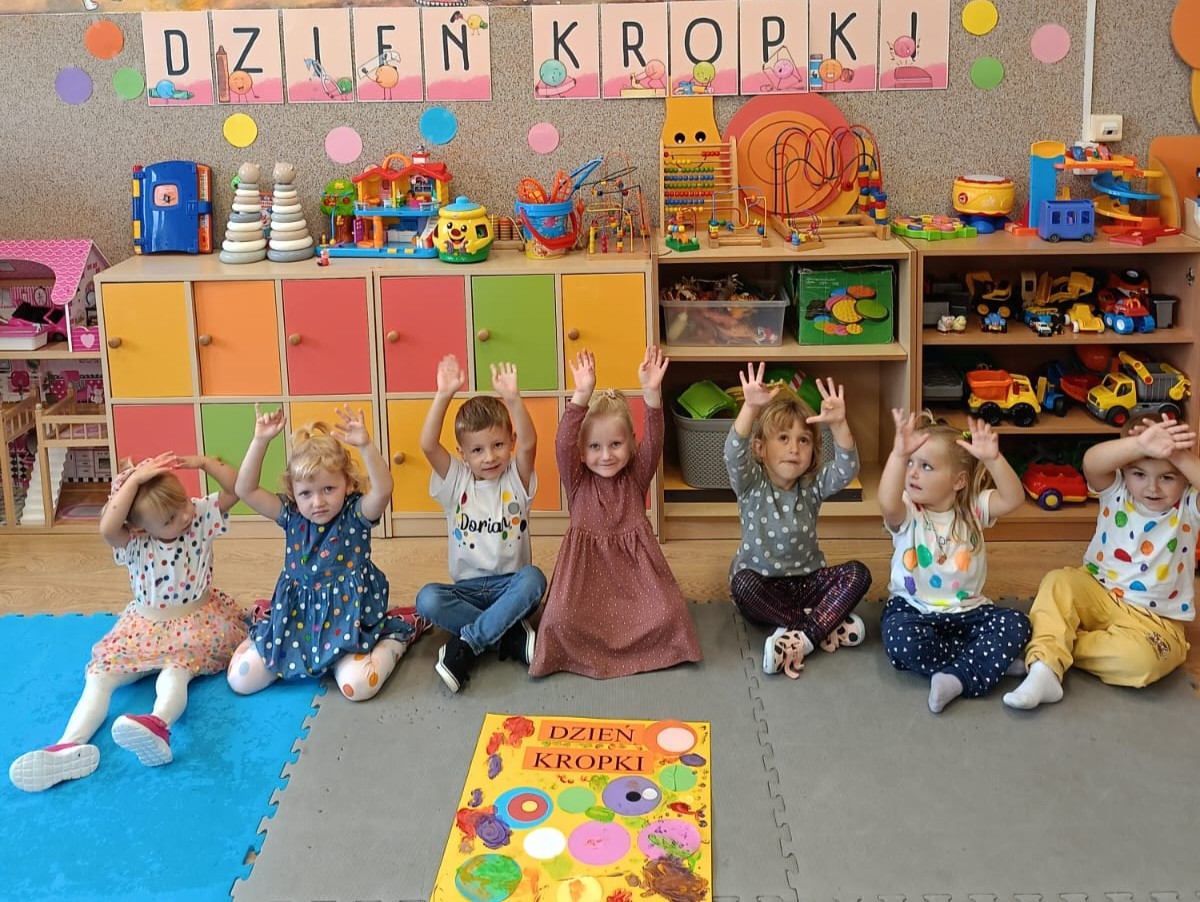 Przedszkolaki siedzą na dywanie przy wspólnym plakacie