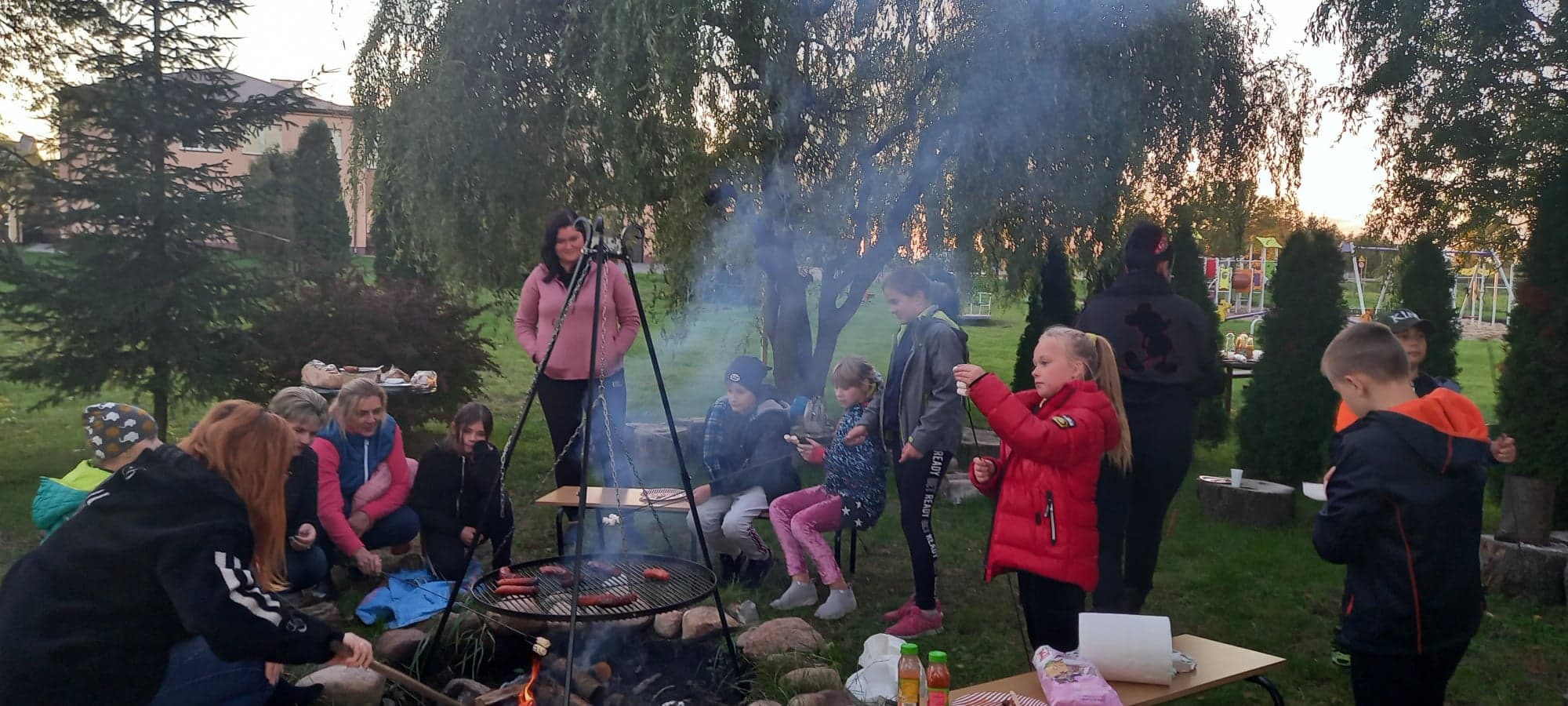 Uczniowie i rodzice przy ognisku spożywają posiłek