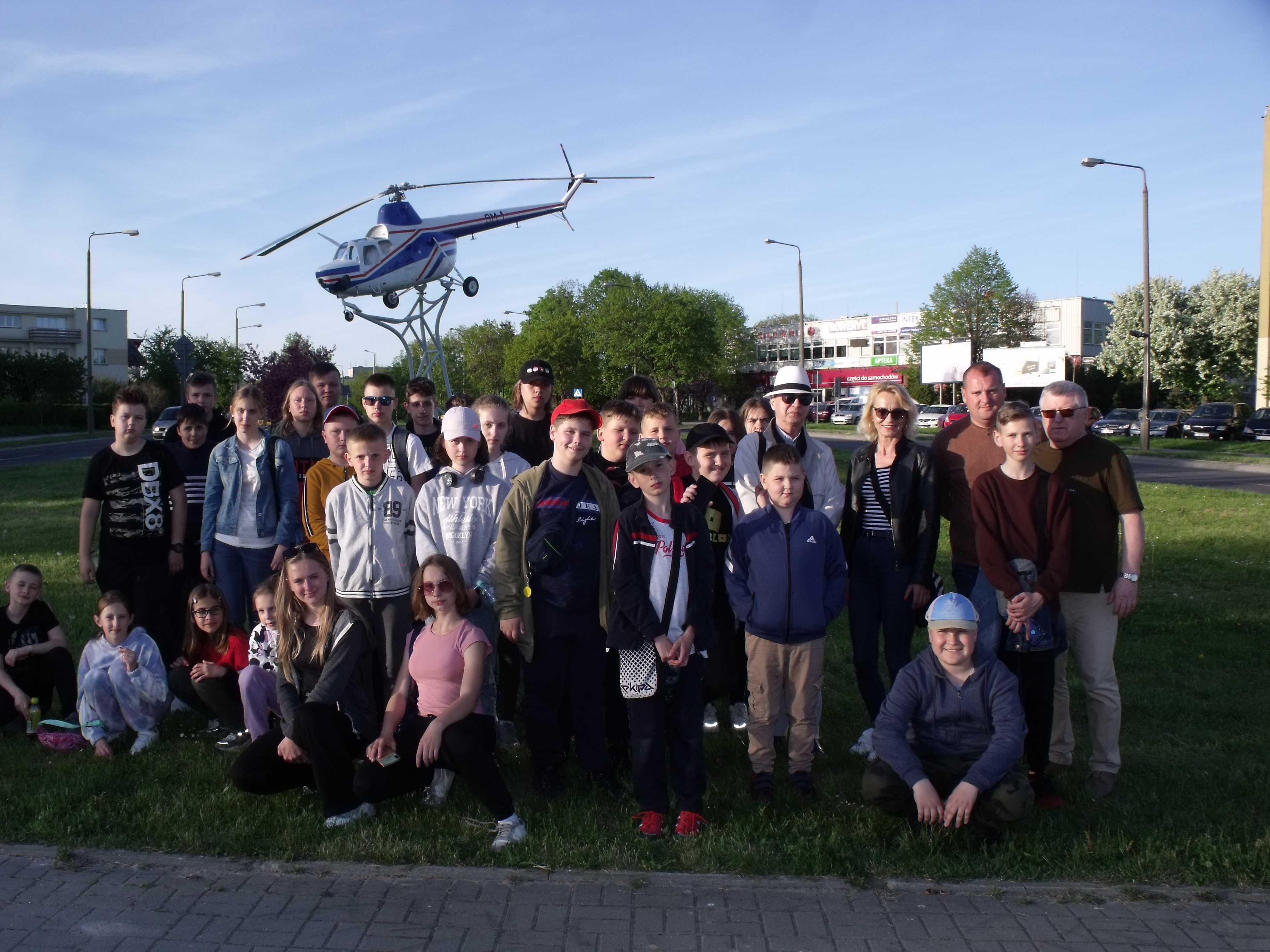 Uczniowie wraz z nauczycielami i przewodnikiem przed helikopterem - symbolem miasta, ustawieni do pamiątkowego zdjęcia
