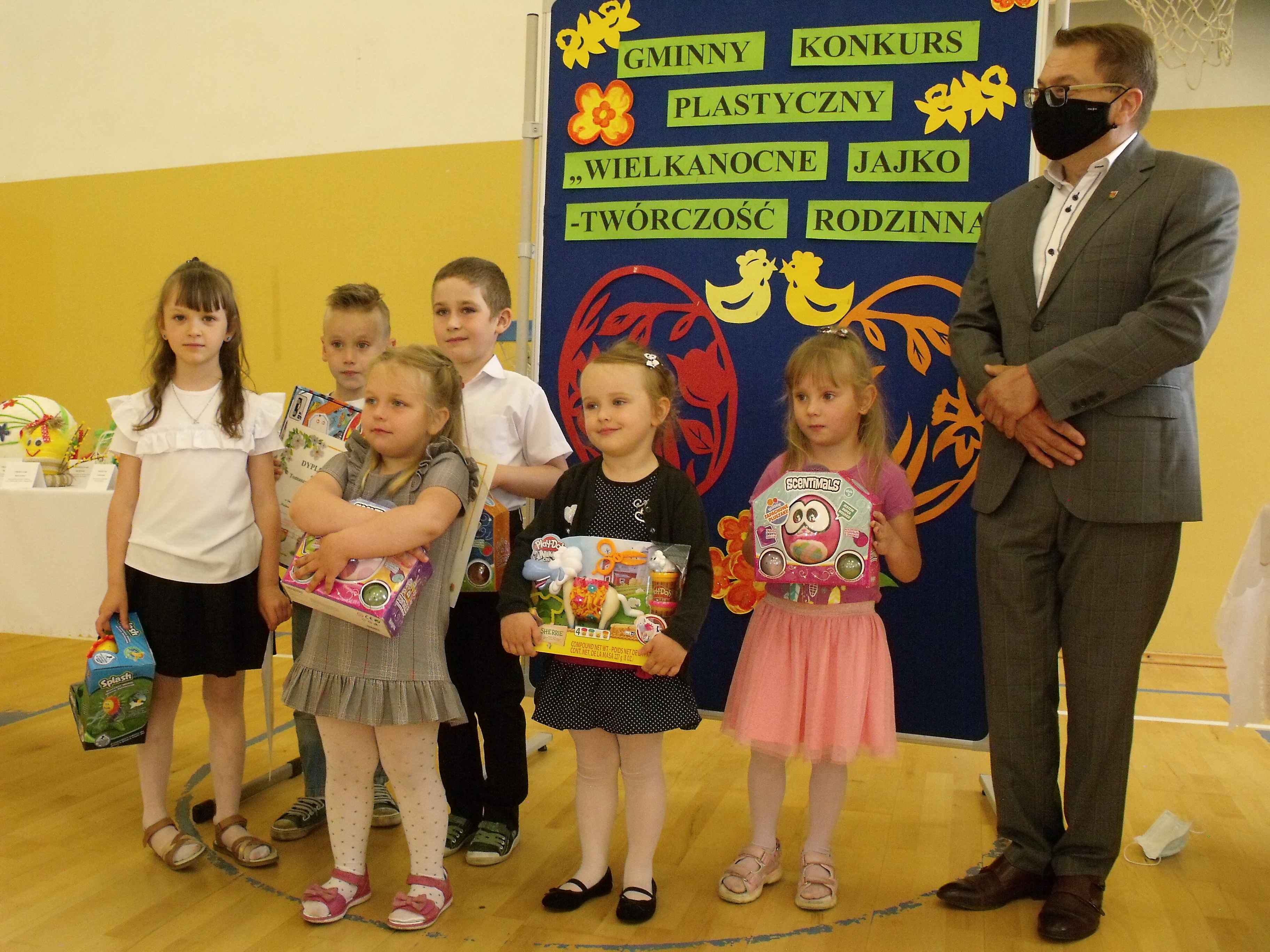 Sekretarz Gminy Hrubieszów oraz cztery dziewczynki i dwóch chłopców trzymających nagrody otrzymane w konkursie.