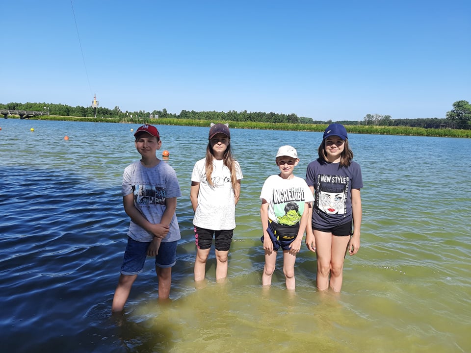 Uczniowie klasy V - dwie dziewczynki i dwóch chłopców stoją po kolana w wodzie zalewu
