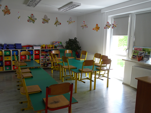Pomieszczenie przedszkolne wyposażone w ławki, stoliki, kolorowe szafki