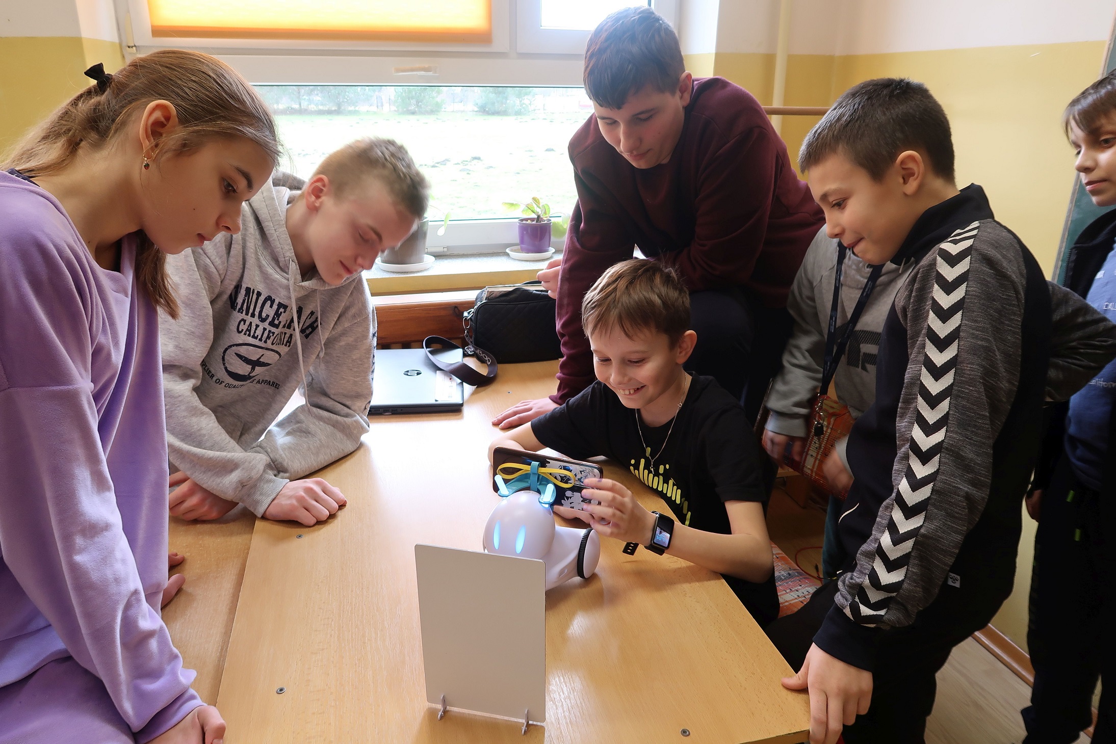 Zdjęcie przedstawia uczniów, którzy grają z robotem w kółko i krzyżyk.