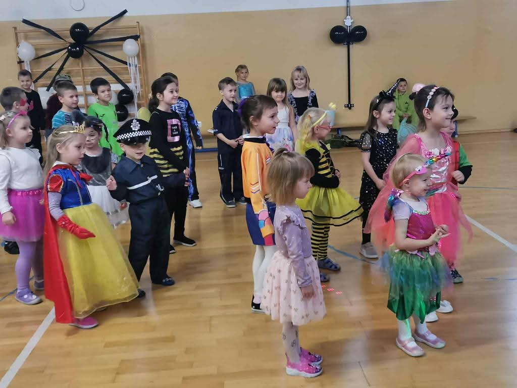 Młodsze dzieci uczestniczące w zabawach tanecznych na sali gimnastycznej.