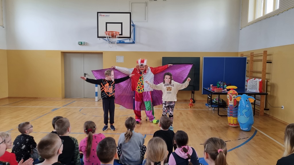 Dwoje dzieci z założonymi maskami śpiewa z klaunem piosenki