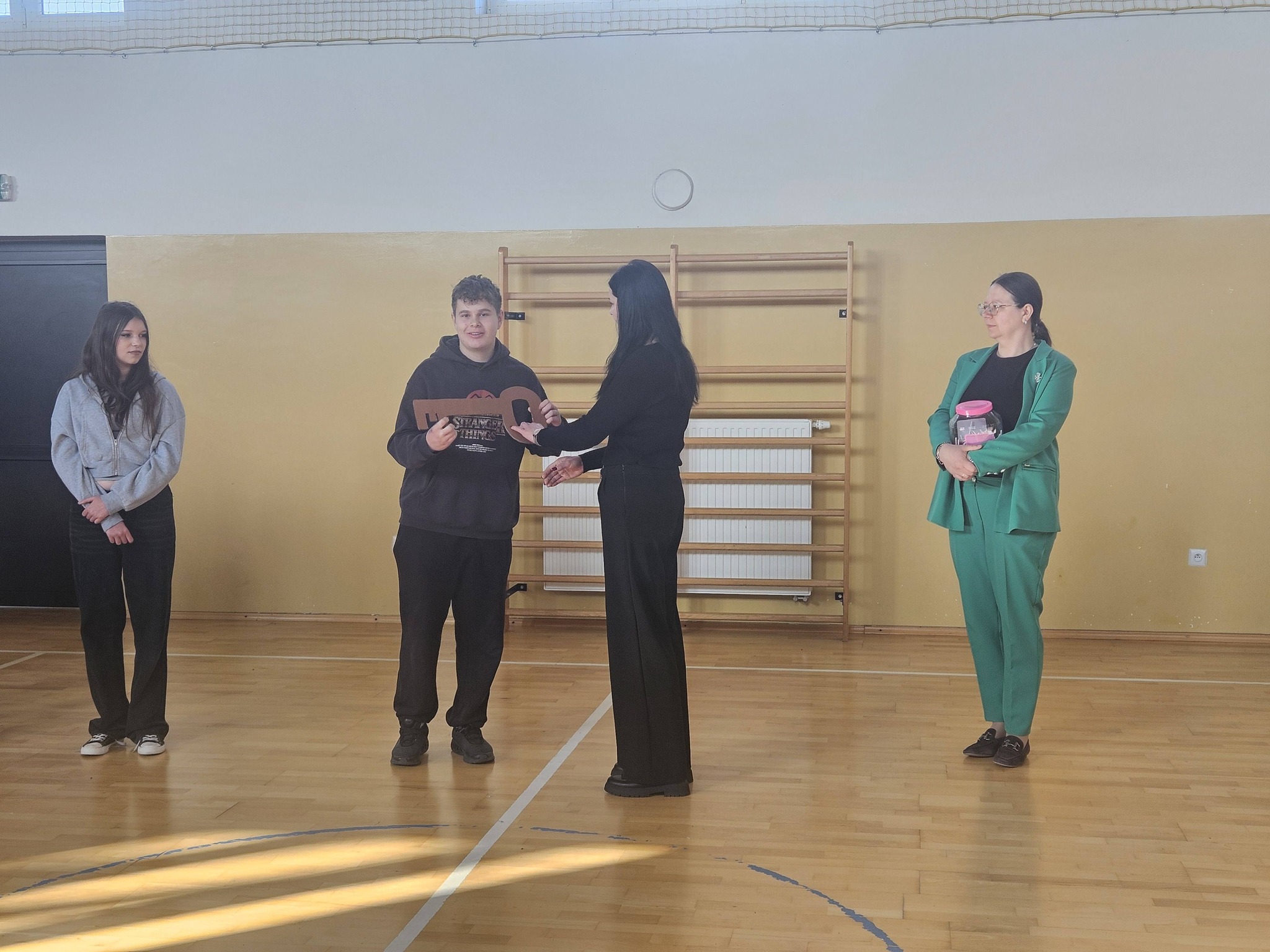 Uczeń odbiera symboliczny klucz podczas apelu, stojąc obok nauczycieli i dyrekcji.