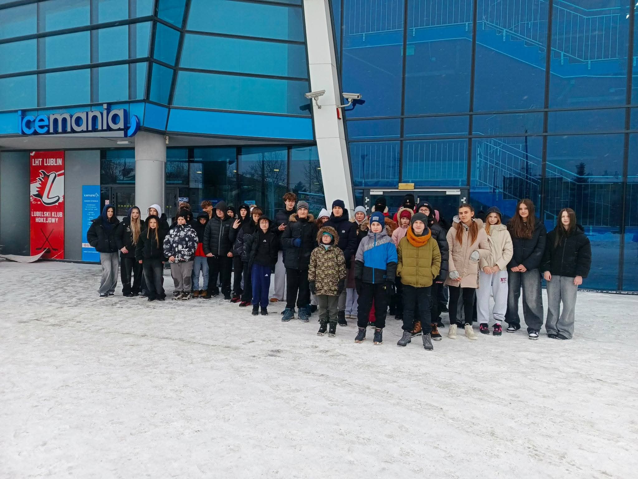 Grupa uczniów stojąca przed budynkiem lodowiska „Icemania” w zimowej scenerii.