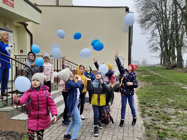 Grafika ilustrująca uczniów wypuszczających do nieba niebieskie balony