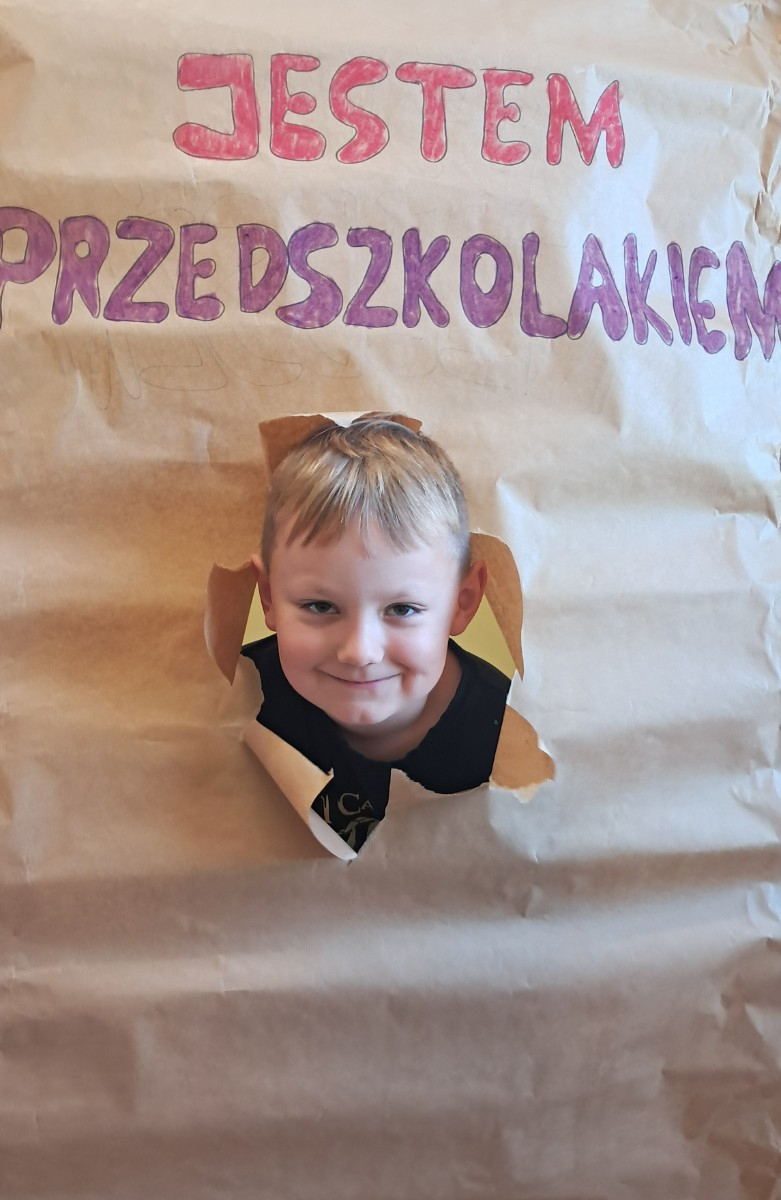 Przedszkolak prezentuje się do zdjęcia z napisem 