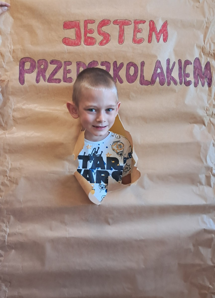 Przedszkolak prezentuje się do zdjęcia z napisem 