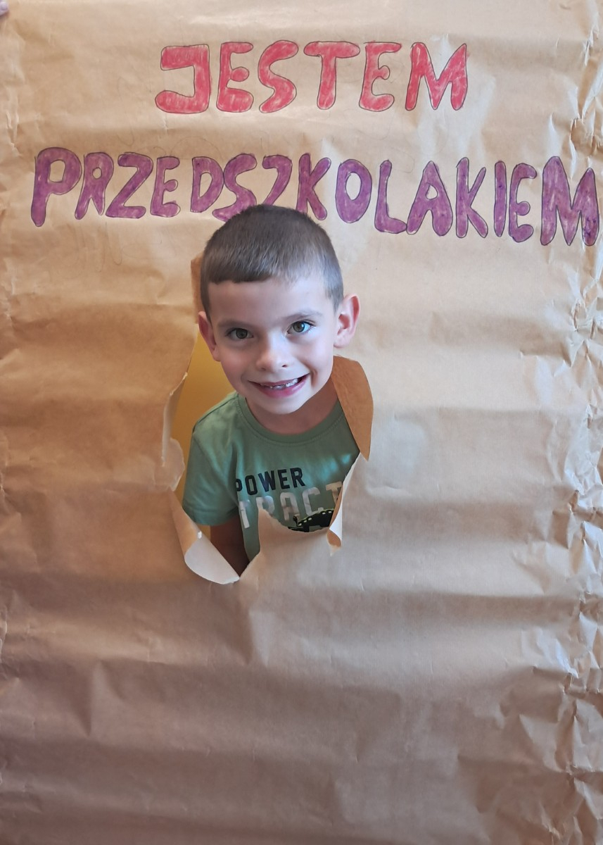 Przedszkolak prezentuje się do zdjęcia z napisem 