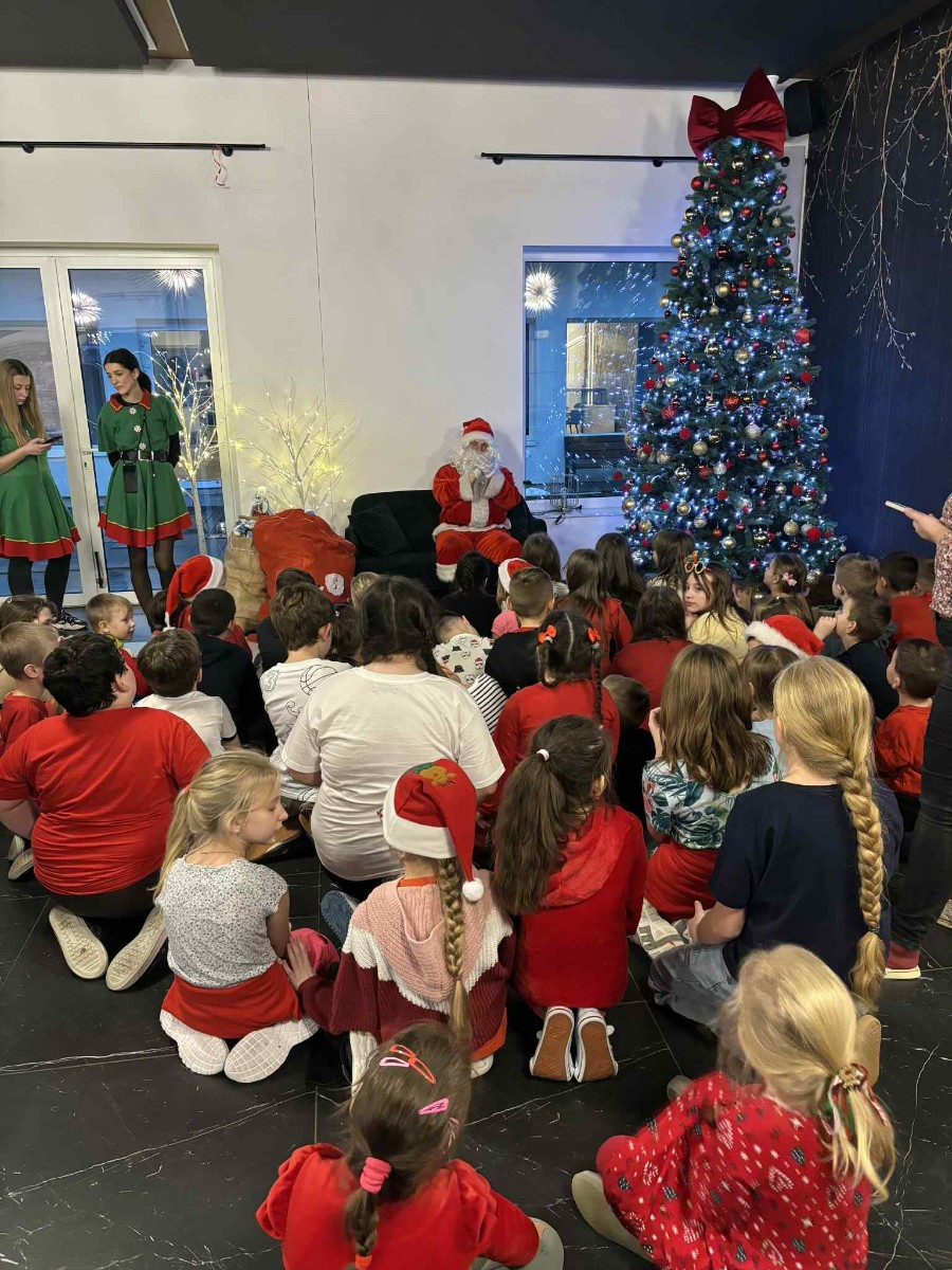 Dzieci pozują do zdjęcia w świątecznej scenerii siedząc przed Mikołajem.