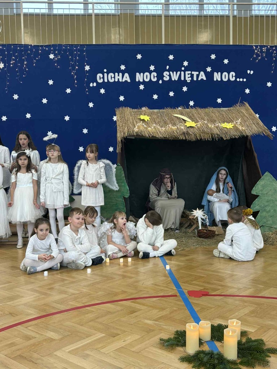 Przedszkolaki siedzą ze świecami przy żłóbku.