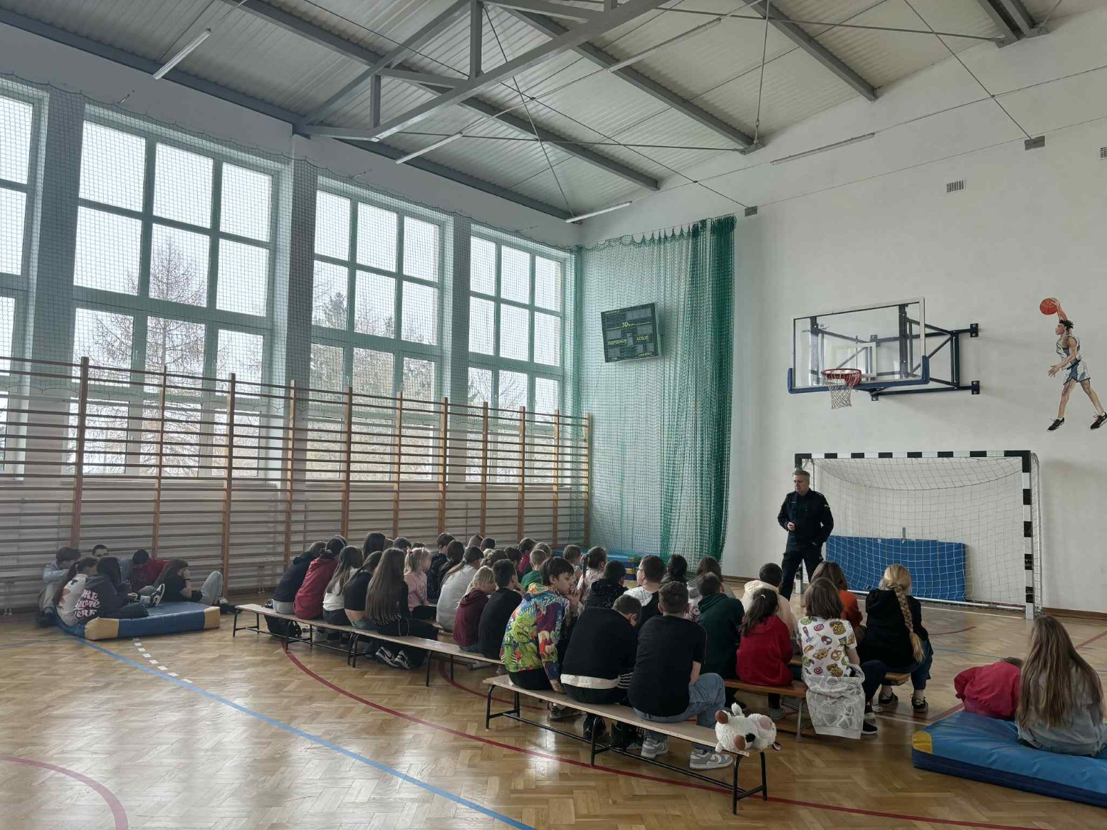 Policjant przekazuje społeczności szkolnej informacje na temat bezpieczeństwa podczas jazdy spacerów oraz ferii zimowych.