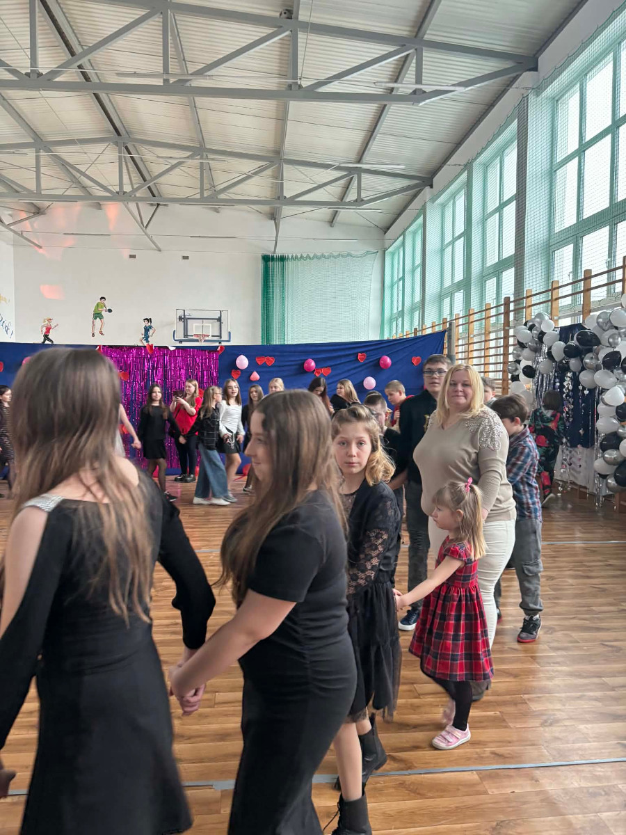 Dzieci wraz z uczniami biorą udział w zabawie choinkowej przy muzyce, a w środku tańczy biały miś.