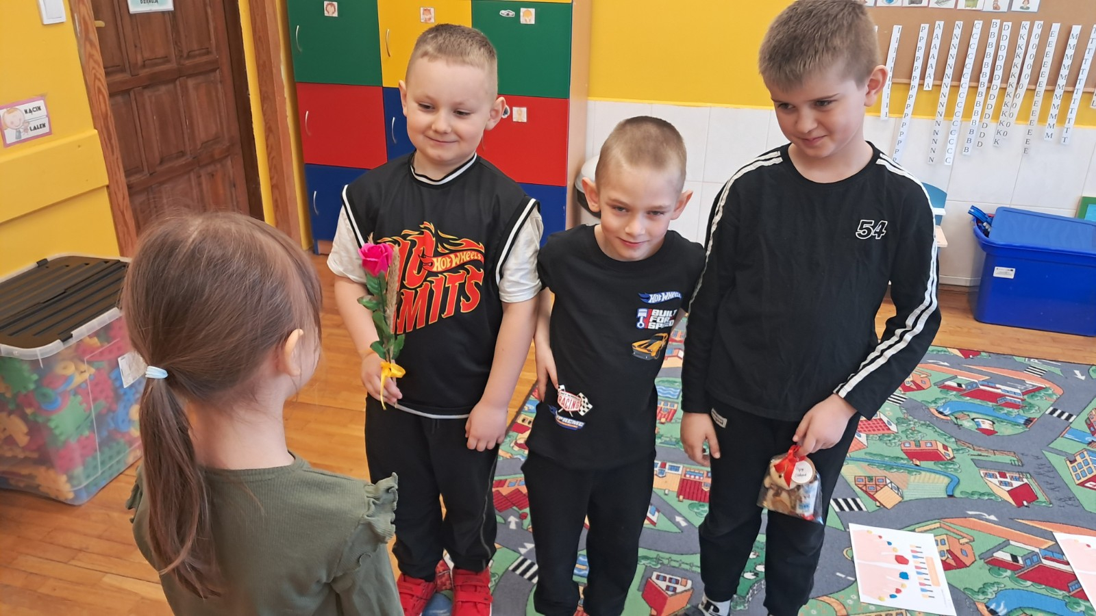 Chłopcy wręczają dziewczynce prezenty.