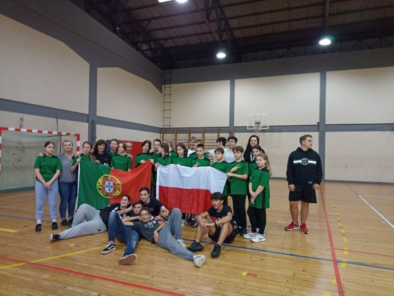 djęcie przedstawia grupę uczniów, którzy znajdują się na sali gimnastycznej, trzymają flagi, Polską i Portugalską.