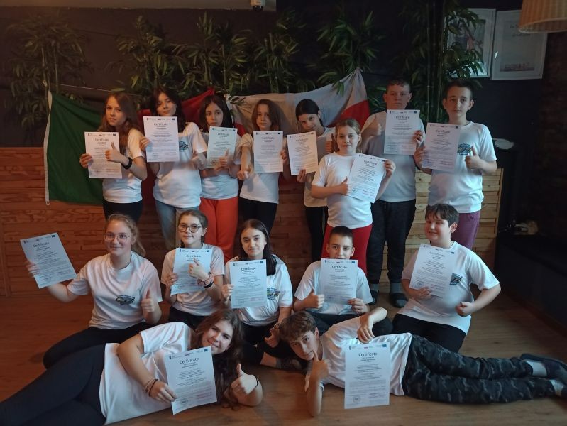 Zdjęcie przedstawia grupę uczniów, którzy trzymają w dłoniach certyfikaty uczestnictwa w projekcie. W tle widać flagi Polski i Portugalii.
