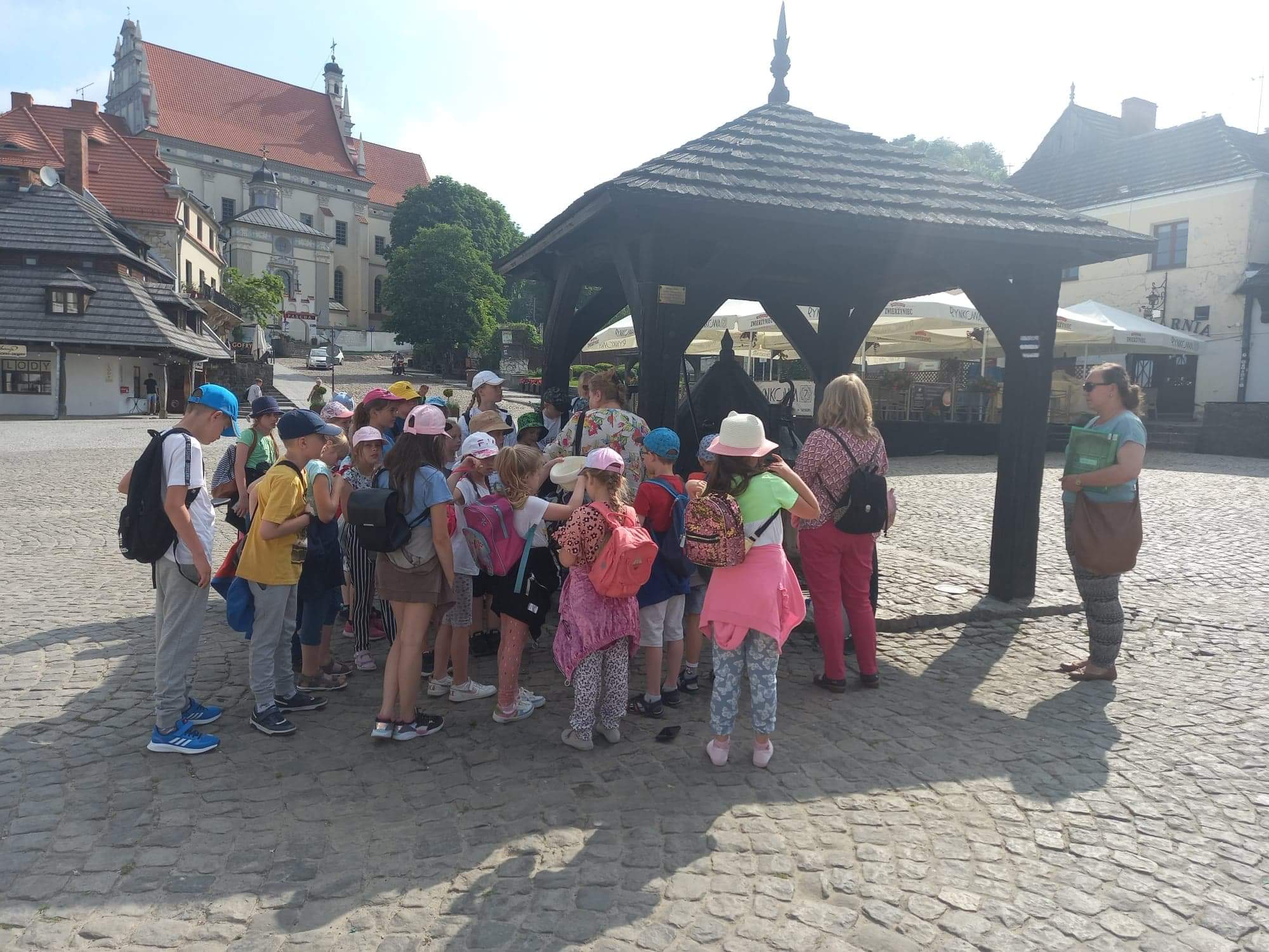 Grafika ilustrująca grupę uczniów z wychowawcą na Rynku w Kazimierzu Dolnym
