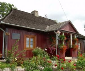 Czerwony drewniany budynek pokryty czarną dachówką, przed budynkiem rosną czerwone kwiaty