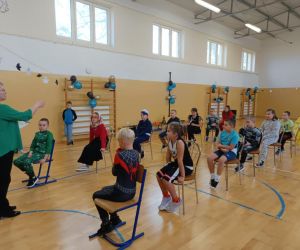  Dzieci siedzące na krzesełkach i wykonujące polecenia nauczyciela w celu wykonania zadania