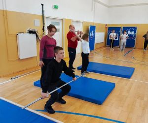 Uczeń i uczennica uczą się techniki podnoszenia sztangi pod okiem trenerów