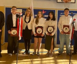 Uczniowie stoją na tle dekoracji z wychowawcą