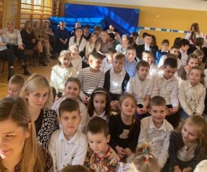 Dzieci z nauczycielami siedzą na ławkach