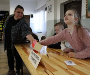 Na zdjęciu widoczne są cztery osoby jedna z nich losuje zadanie konkursowe.