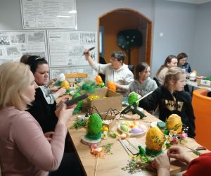 Na zdjęciu widoczna jest grupa uczestników warsztatów wielkanocnych, wykonująca stroiki.