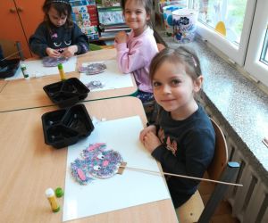 Na zdjęciu widoczne są dzieci siedzące w ławkach i wykonujące prace plastyczną.