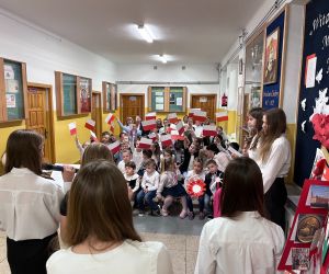 Uczennice śpiewają piosenki patriotyczne , młodsi uczniowie machają flagami