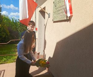 Dwoje uczniów składa kwiaty i znicz pod tablicą patrona szkoły