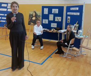 Pani Dyrektor przemawia do społeczności szkolnej, w tle dwoje uczniów przy dekoracji okolicznościowej