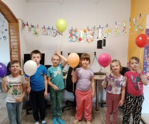 Na zdjęciu widoczne są dzieci pozujące do zdjęcia  wewnątrz budynku wraz z kolorowymi balonami.
