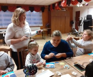 Zdjęcie przedstawia dzieci wraz z rodzicami wykonujące kartki okolicznościowe dla nauczyciela.