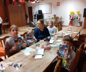 Zdjęcie przedstawia dzieci wraz z rodzicami wykonujące kartki okolicznościowe dla nauczyciela.