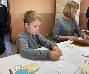 Dzieci podczas warsztatów organizowanych przez GOK, wewnątrz budynku, wykonują kartkę metoda scrapbookingu.