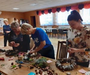 Panie wykonują dekoracje na drzwi - wieniec z szyszek.