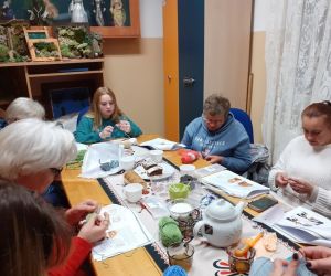 Grupa pań wewnątrz budynku szyje na szydełku.