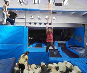 Uczeń klasy ósmej podciąga się na linach nad basenem z piankowymi kostkami