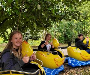 Dwie uczennice i jeden uczeń w wagonikach kolejki. Wagoniki stylizowane na żółte kaczuszki