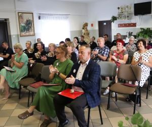 Na zdjęciu widoczni są zaproszeni goście, siedzący na krzesłach, wewnątrz budynku.