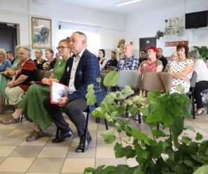 Zdjęcie przedstawia grupę osób siedzących na krzesłach, wewnątrz budynku.