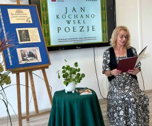 Nauczycielka matematyki czyta poezję, siedząc na tle dekoracji okolicznościowej