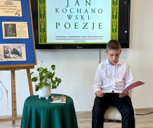 Uczeń klasy piątej czyta poezję, siedząc na tle dekoracji okolicznościowej
